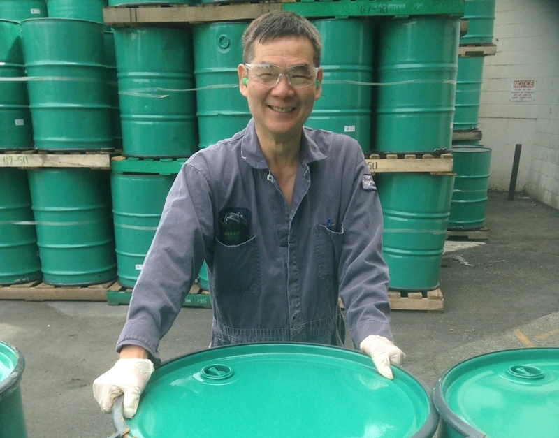 Smiling manufacturing employee in front of teal Tremco waterproofing barrels 