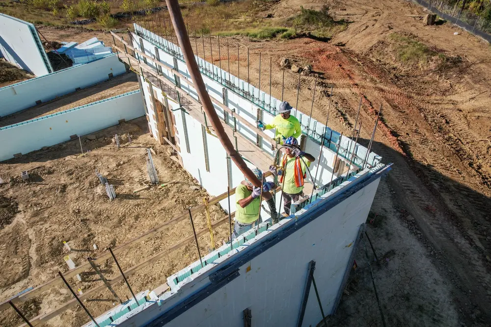 Construction workers spray concrete into Nudura insulated concrete form building. 