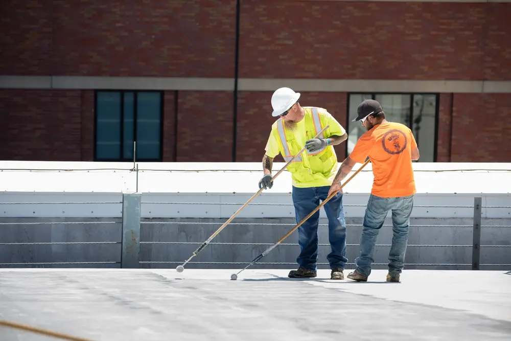 Two construction workers applying Tremco roof restoration products with rollers on a roof deck. 