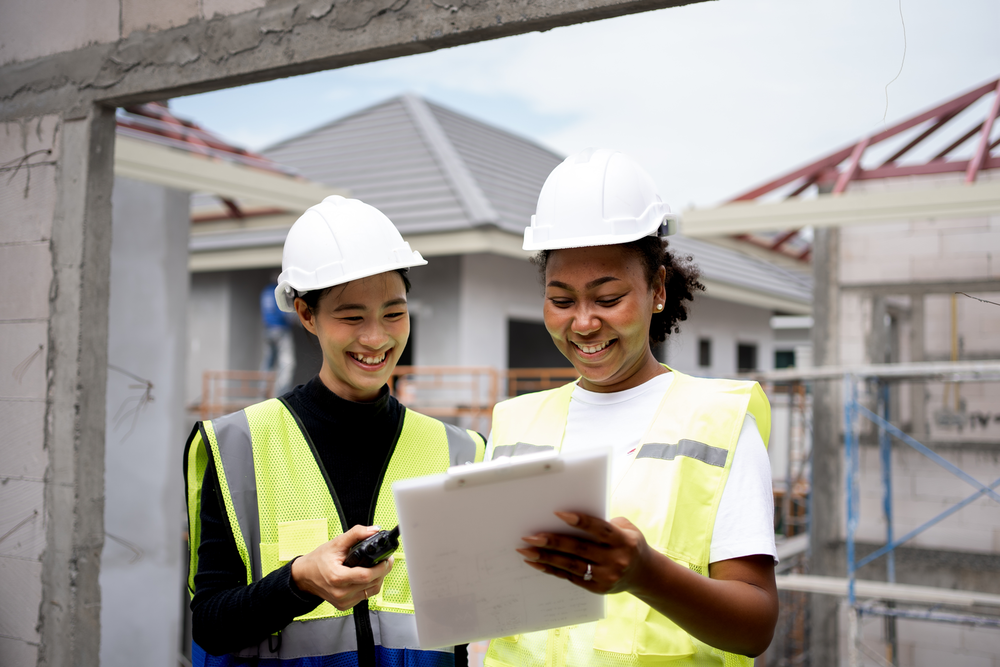 2 female construction workers smile and look at a clipboard