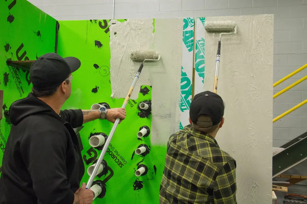 Two male workers rolling gray air barrier on wall