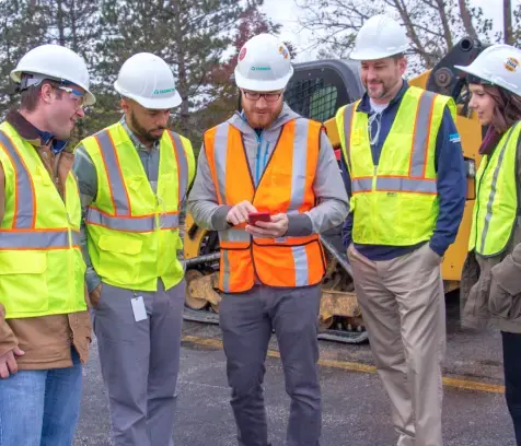 Five construction workers talking on a construction site with safety vests and hard hats