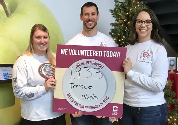 3 Tremco employees smiling and holding volunteer sign at House for Hunger